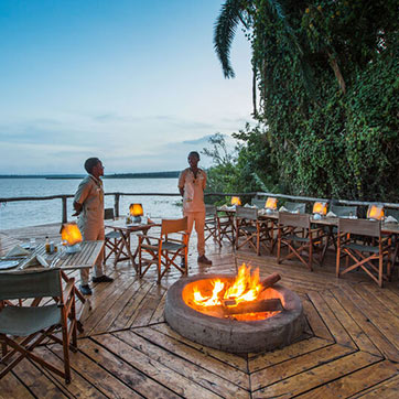 Two gentleman standing by a fire awaiting guests at the dining area in Akagera National Park
